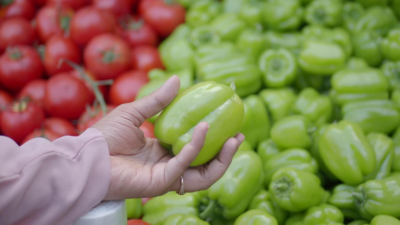 una mano sostiene un pimienta verde en un puesto de productos