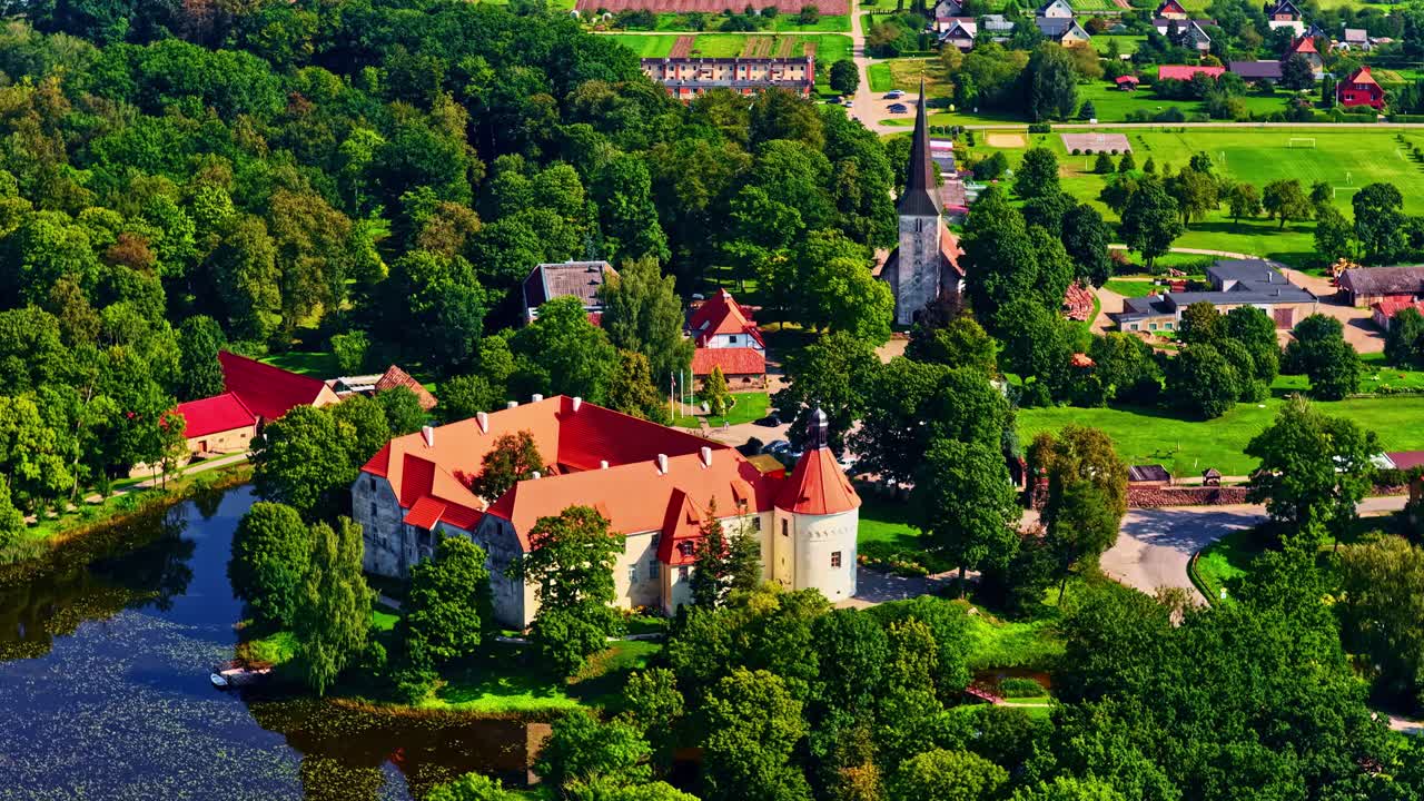 Panoramica aerea del Castello di Jaunpils circondato da un lago e vegetazione in Lettonia, paesaggio di un villaggio medievale.