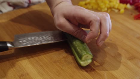 close up on steel knife slicing green cucumber on wooden cut board