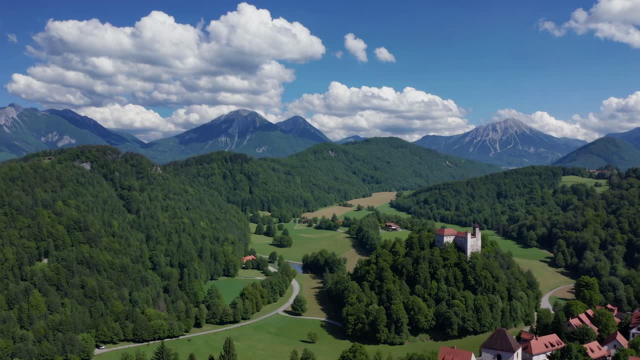 Aerial video captures a scenic landscape with lush forests, a quaint village, and distant mountains