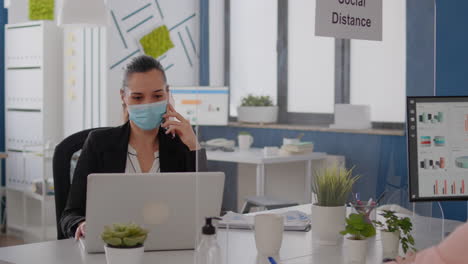 woman with protective face mask working on laptop computer in company office