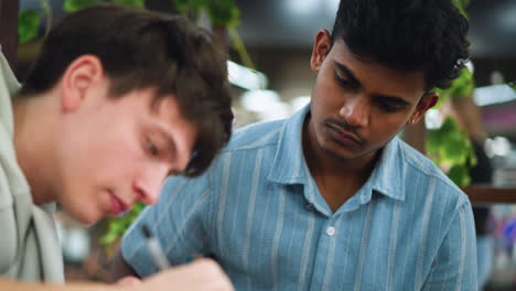 teenager in blue shirt sitting beside colleagues and looking proudly at detailed sketches while nodding in approval during collaborative art workshop under warm lighting creative atmosphere
