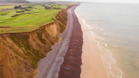 Aerial---Coast-and-cliffs-on-North-Sea,-Sheringham,-England,-wide-backward-shot