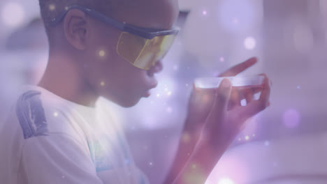 animation of light particles over african american schoolboy studying petri dish in science class