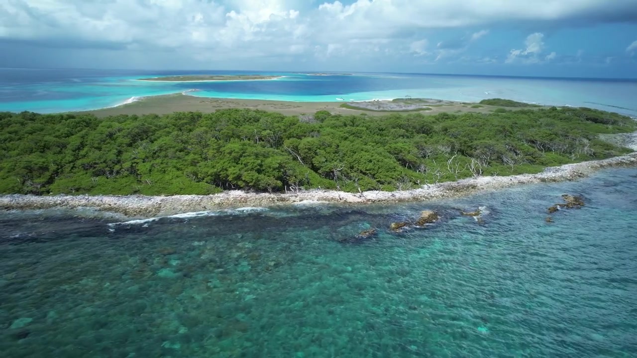Isola tropicale con vegetazione lussureggiante circondata da acque cristalline turchesi sotto un cielo parzialmente nuvoloso