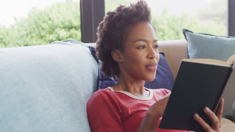 Video-of-african-american-woman-reading-book-on-sofa