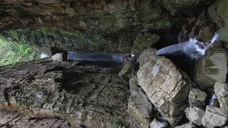 vertical format aerial pull-in to waterfall in narrow rock cliff gorge