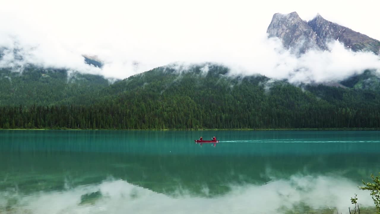 dos personas en kayak en un hermoso lago azul pacífico con enormes montañas rocosas nubladas en el fondo y reflexión sobre el lago, parques nacionales de canadá