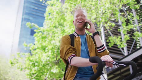 Happy-albino-african-american-man-with-dreadlocks-in-park-with-bike-talking-on-smartphone