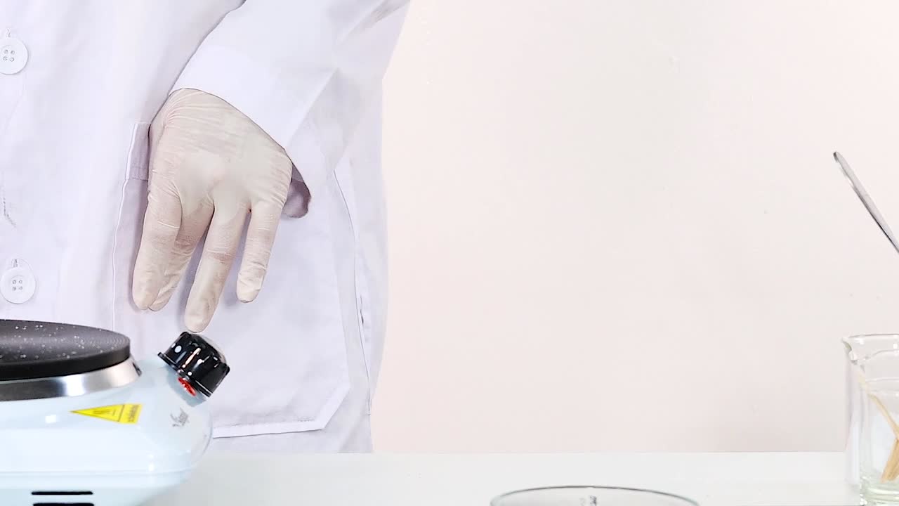 A scientist in a lab coat demonstrates using a beaker and hot plate.