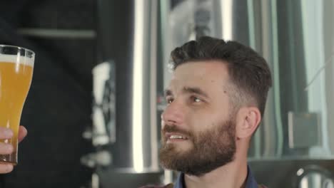 young brewer wearing a leather apron is tasting beer at a modern brewery