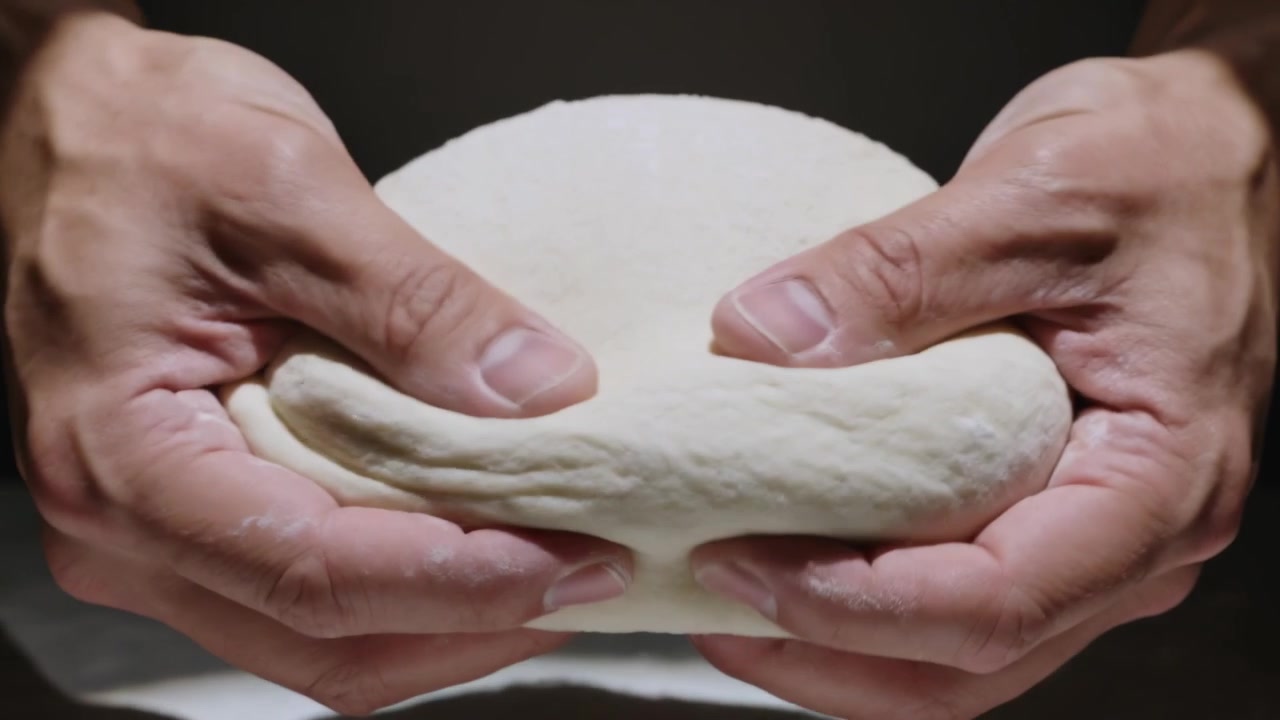 Pressing adult hands pinching and tucking dough at kitchen countertop, forming taut dome for baking
