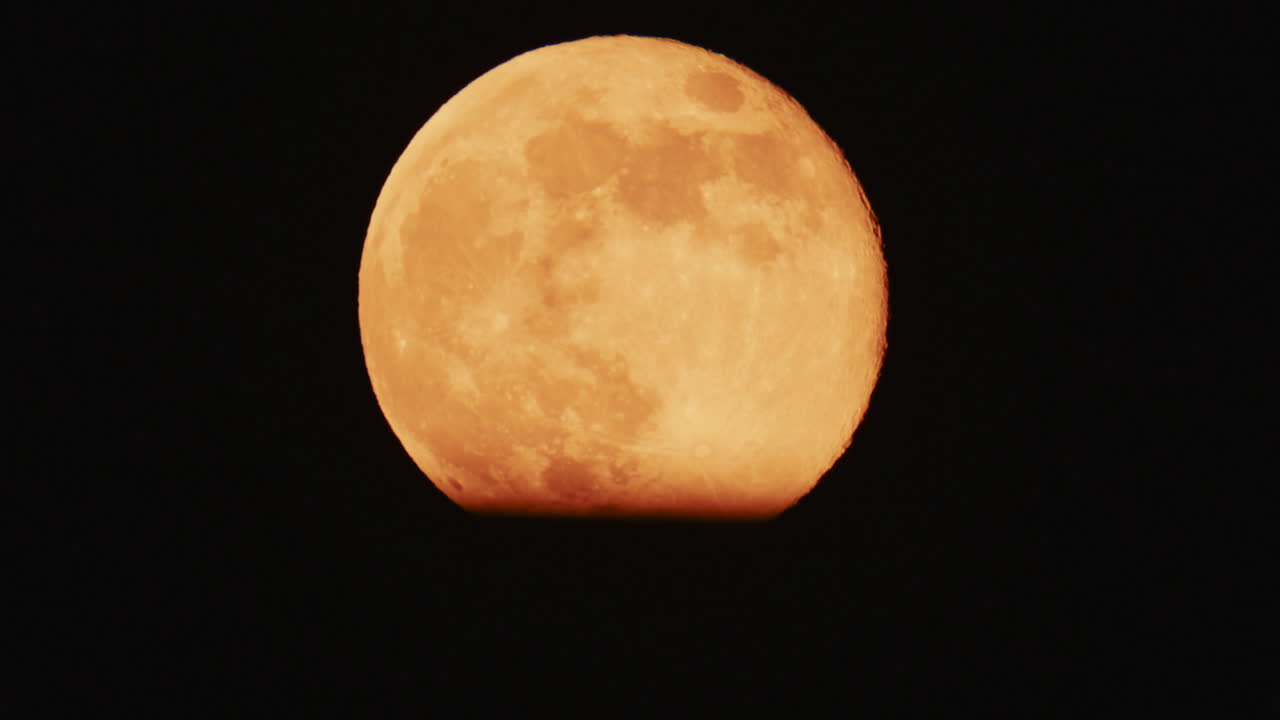 Large full moon rising against a dark night sky with clear details and dramatic atmosphere