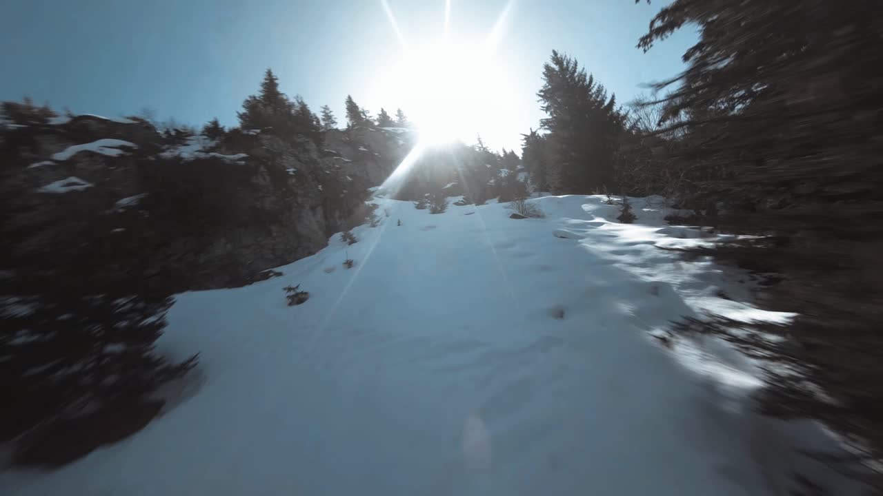 Drone FPV cinematografico a bassa quota che vola lungo il fianco di una montagna innevata.