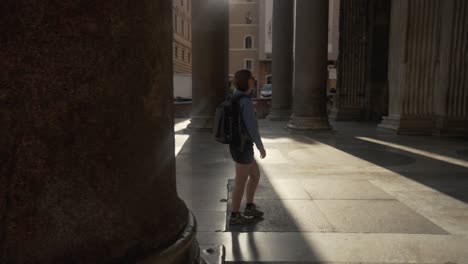 pan shot of a woman walking between the pillars of the pantheon with the sun coming through in rome in 4k