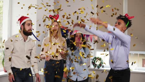 group of multi-ethnic office workers partying in the office throwing golden confetti, blowing confetti from hands wearing