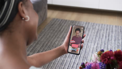 mujer afroamericana sosteniendo un teléfono inteligente con un hombre afroamericano con un regalo en la pantalla