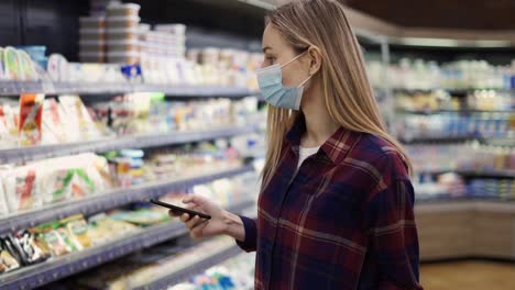 mujer tomando leche en el supermercado usando teléfono inteligente, comprobando la lista de compras