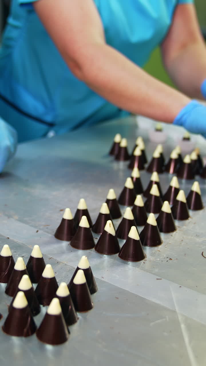 Confectionery worker extracts candies from molds. Other worker puts ready-made sweets into a packaging paper. Close up. Vertical video