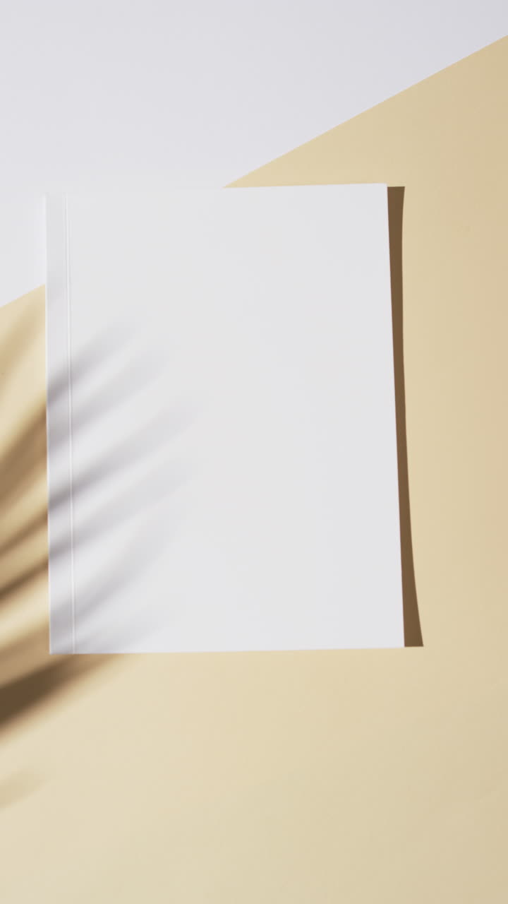 Vertical video of shadow over book with blank pages and copy space on yellow background