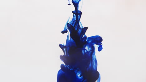 video en cámara lenta de tinta de acuarela azul mezclándose en agua contra un fondo gris