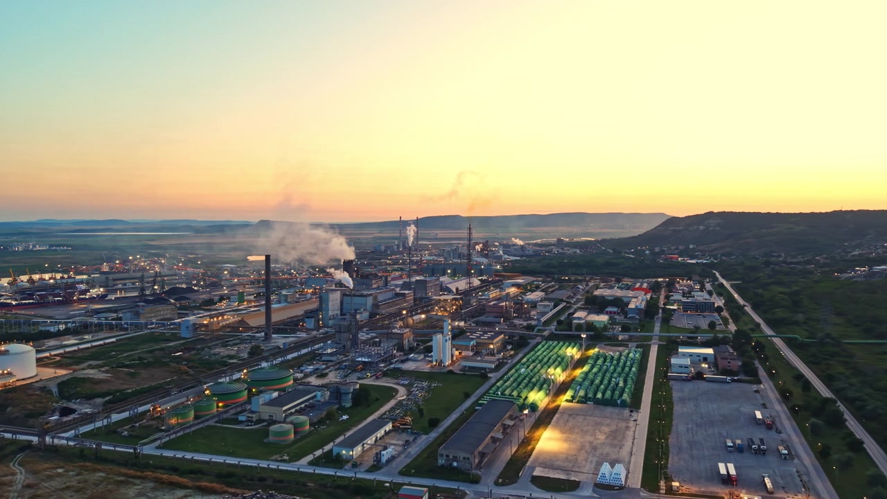 Industrial site during sunset with smoke rising and machinery visible in the background