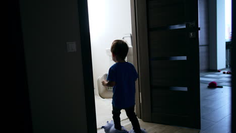 Little child heading to the bathroom carrying a prop. Kid in funny slippers approaches the faucet and opens water.