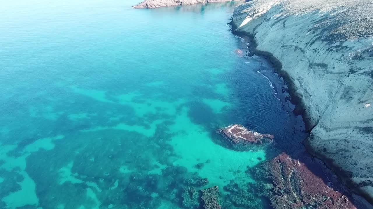 Cinematic drone shot capturing the rugged texture of a steep coastal mountain slope meeting the deep blue Mediterranean waters, with dramatic shadows