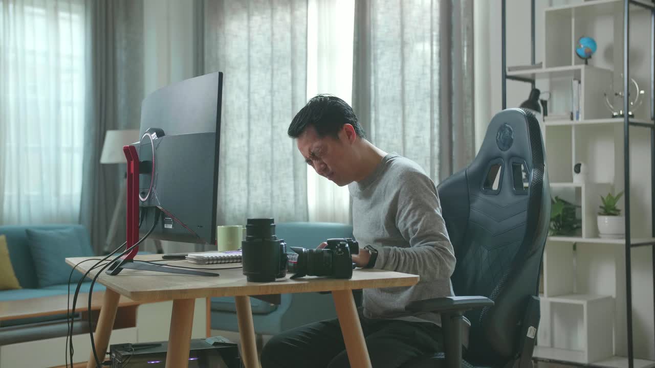 Asian Cameraman In Long Sleeved T-Shirt And Black Pants Having Backache While Using Desktop Computer For Working At Home.