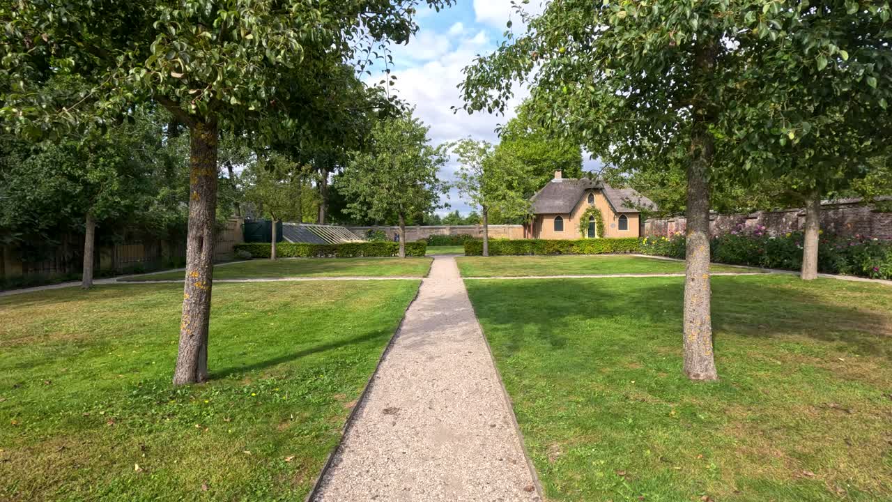Forward camera glides along gravel garden path toward a thatched cottage in lush daylight landscape