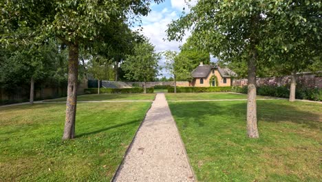 forward camera glides along gravel garden path toward a thatched cottage in lush daylight landscape