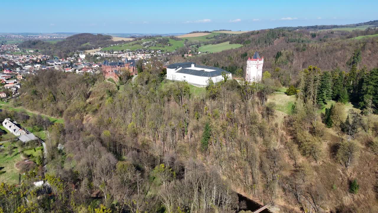 Gradvis bevegelse bakover når drone avslører Hradec nad Moravicí slott i Tsjekkia med skogkledd ås, nærliggende by og vidt landskap som strekker seg ut i det fjerne