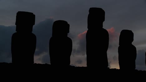 a long line of statues is silhouetted on easter island in this dusk shot