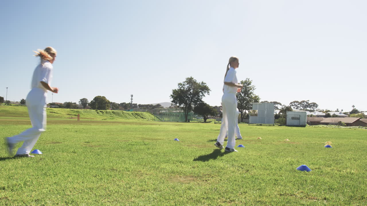 Running drills on grass field, women in white uniforms training for cricket