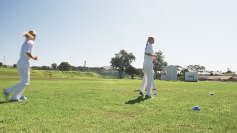 running drills on grass field, women in white uniforms training for cricket