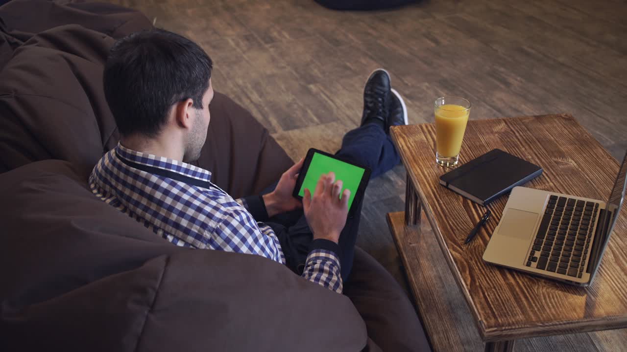 A man sits on the tablet, the tablet on a green screen