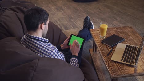 a man sits on the tablet, the tablet on a green screen
