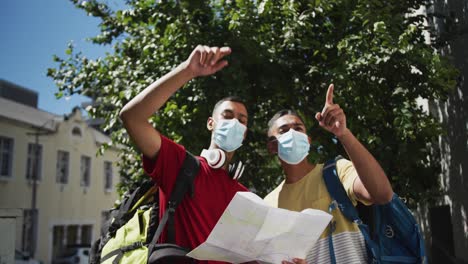 dos amigos varones de raza mixta con máscaras faciales usando un mapa en la calle