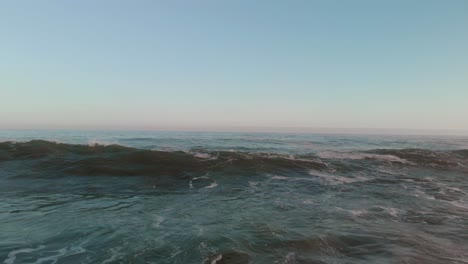 Drone-flying-low-over-open-waters-with-bamboo-floating-on-the-surface-as-swells-and-waves-come-in-and-break