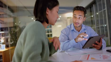 Focused-diverse-male-and-female-colleague-discussing-work-and-using-tablet-late-at-office