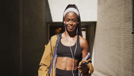 Portrait-of-african-american-woman-exercising-outdoors-wearing-earphones-and-smiling-to-camera