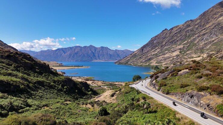 Video 4K con drone di un gruppo di motociclisti Māori che guidano lungo la strada a Lake Hawea a Wanaka, Nuova Zelanda. Le strade si snodano attorno a colline e montagne accanto al lago blu, vasto e sconfinato