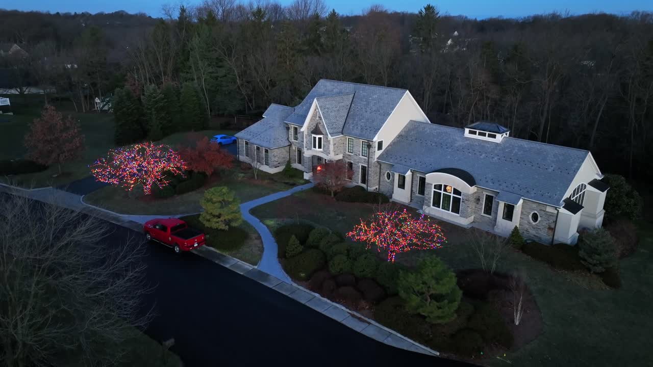 aproximación aérea de la villa de los suburbios durante la época de navidad. árboles decorados con luces en el patio delantero. mansión de granja de lujo en virginia, estados unidos. aparcamiento de coche rojo en la calle.