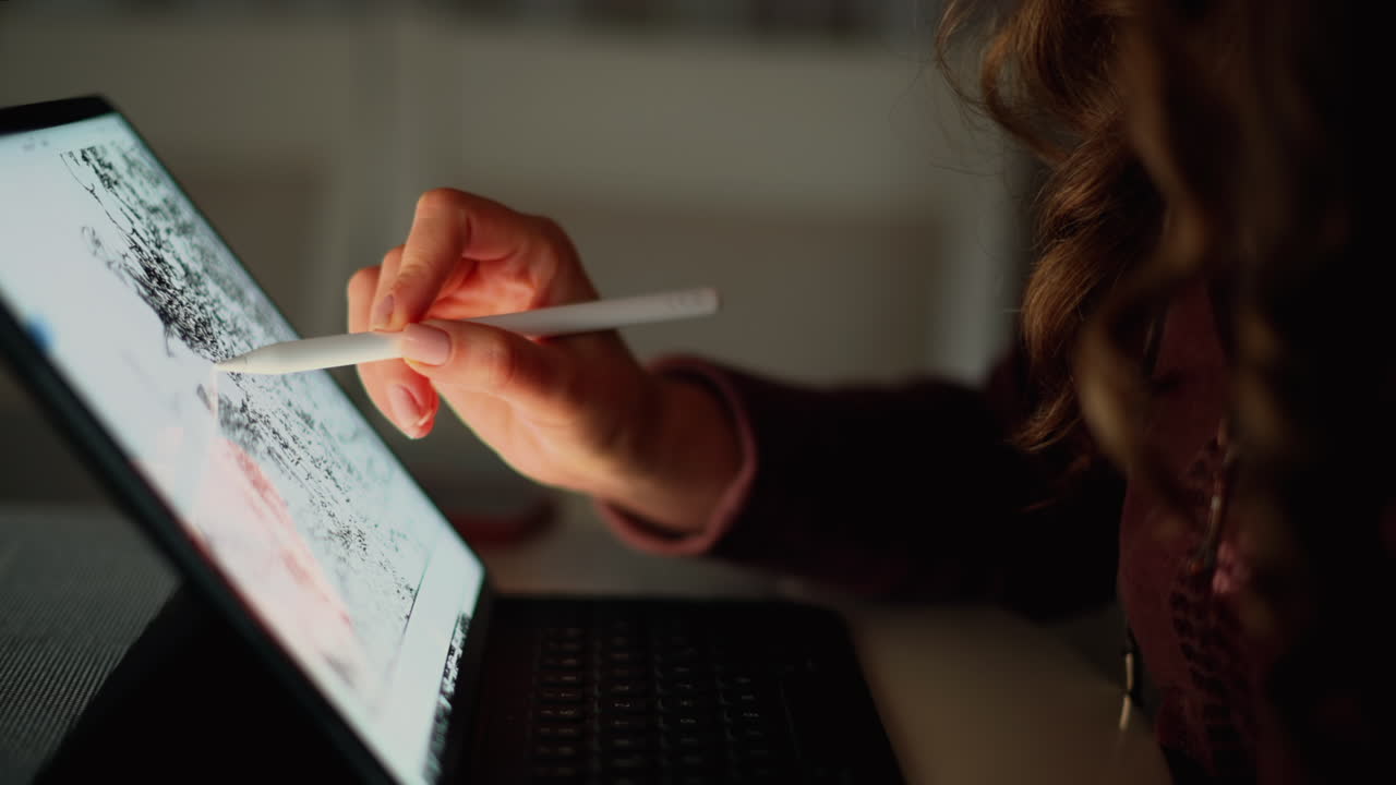 Close up of a woman sketching on a tablet with a stylus pen in the evening