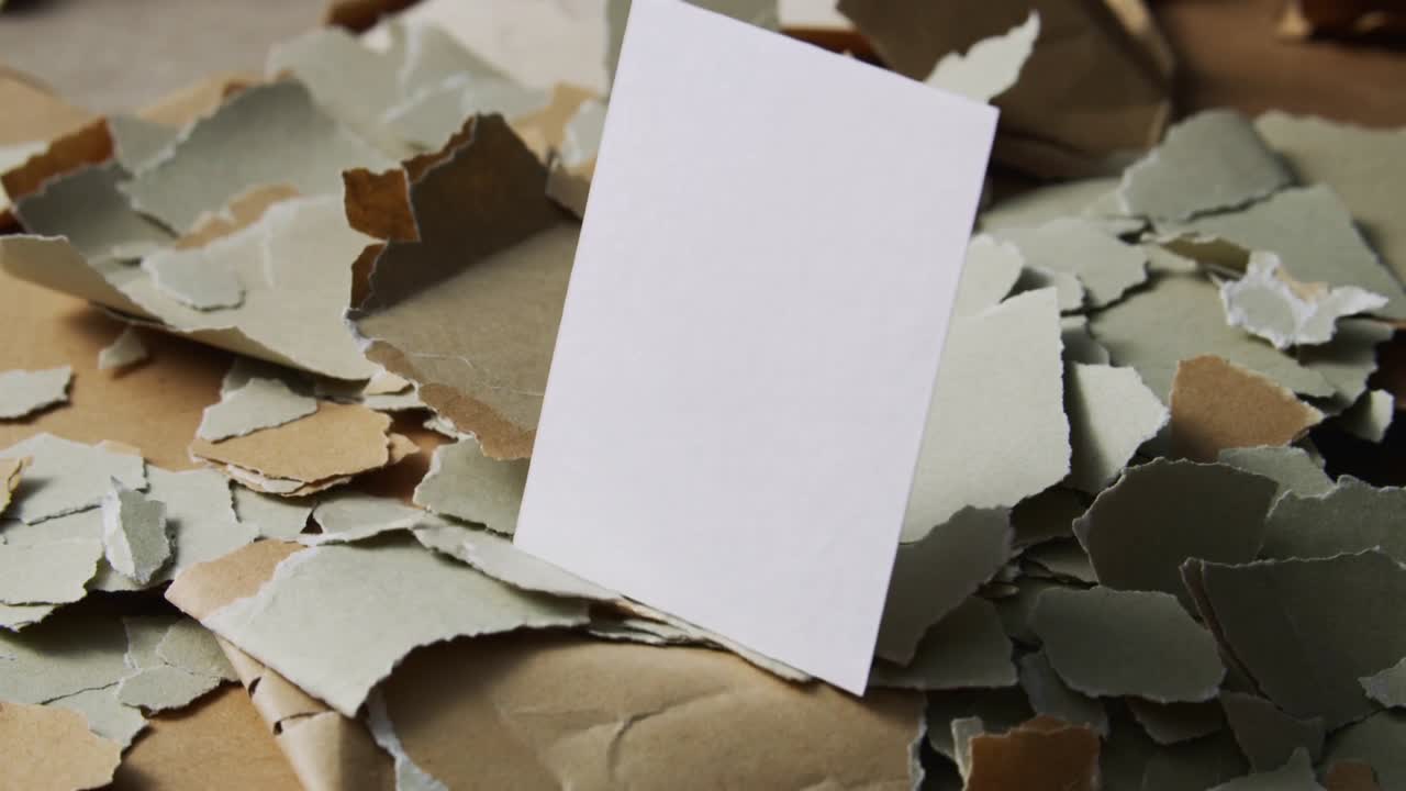 Dropping white card descending onto craft table, shifting torn paper and brown cardboard pieces