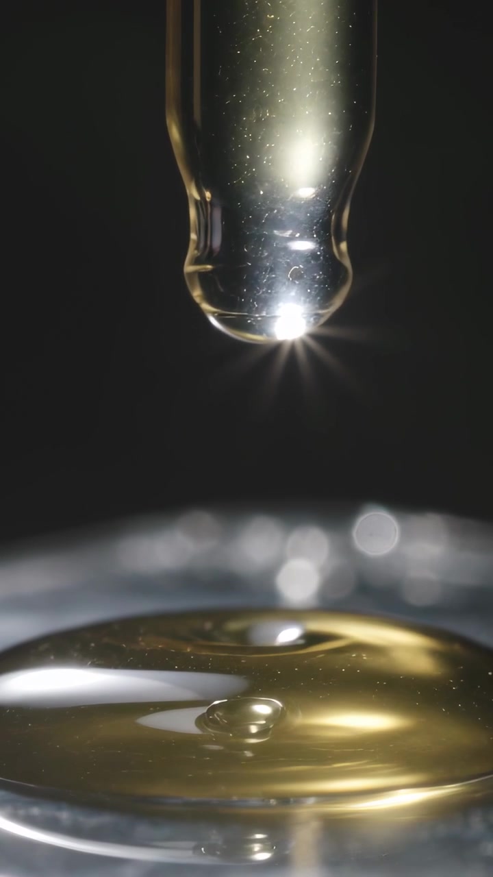 Vidéo verticale: Pipette en verre s'abaissant, laissant tomber de l'huile dorée sur une plaque en studio, formant des perles pour l'étude