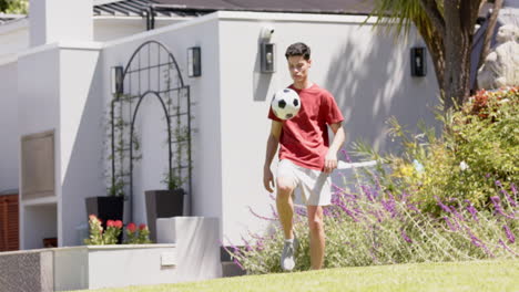 Hombre-Birracial-Enfocado-Haciendo-Malabarismos-Con-El-Fútbol-Con-Muslos-En-Un-Jardín-Soleado,-Espacio-Para-Copiar,-Cámara-Lenta