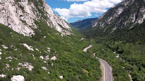 aerial backwards flight showing beautiful mountains and road in green valley during sunlight - washington, mount olympus hillside