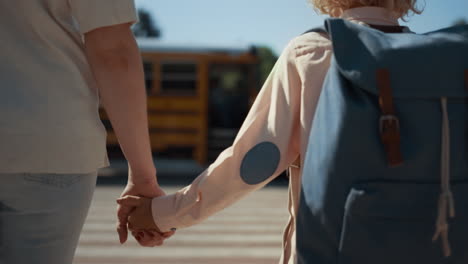 mother holding son hand walking together to schoolbus sunny morning close up.