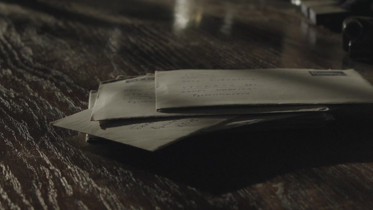 Stack of brown stamped envelopes scattered across a dark tabletop in dramatic low light, creating a retro communication concept associated with payment demands.